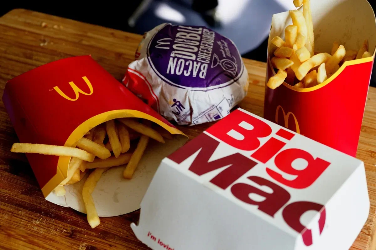  Combo do McDonald's com batatas fritas, hambúrguer Double Bacon Cheeseburger e Big Mac sobre uma tábua de madeira, representando refeição de fast food.